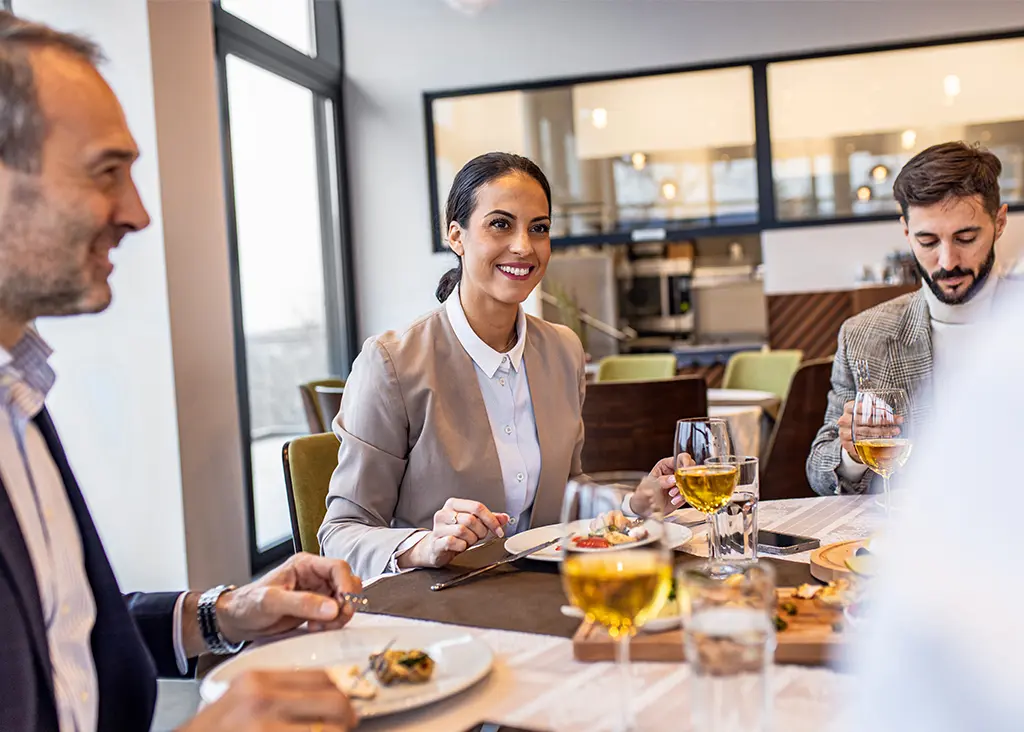 Three colleagues enjoy a meal and drinks together at a modern restaurant table.