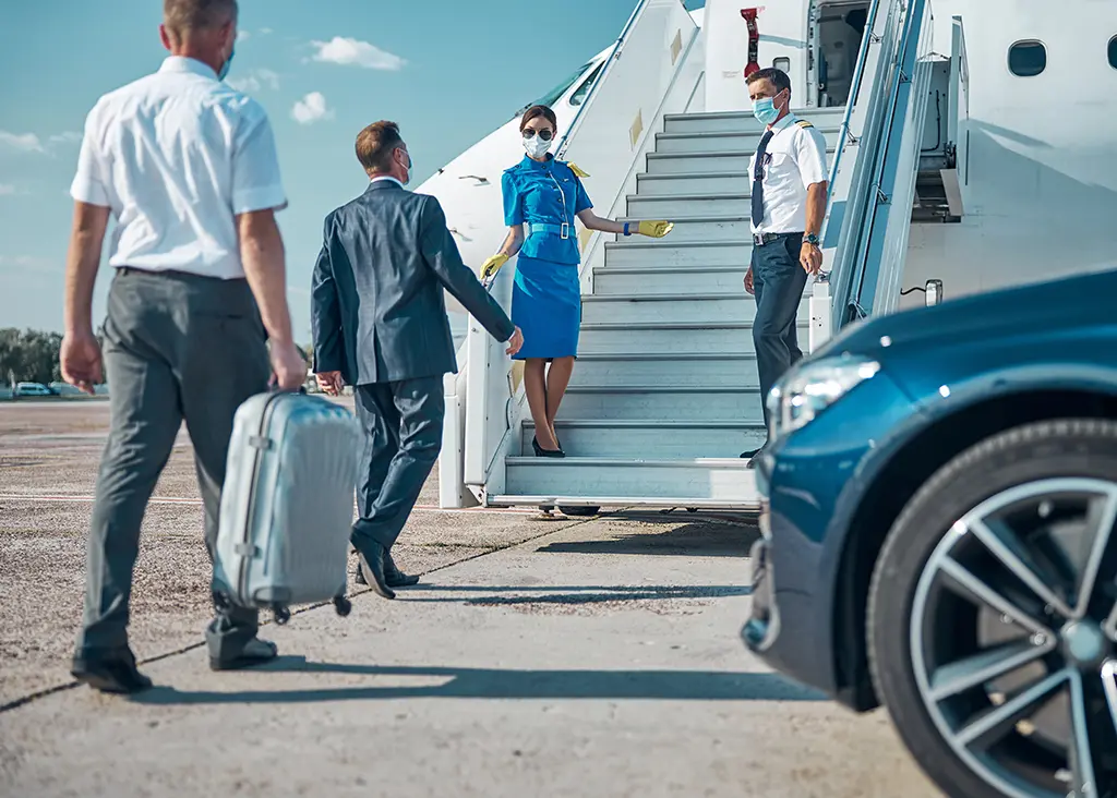 Travelers boarding a private jet with assistance from a pilot, flight attendant, and ground staff beside a luxury car, demonstrating premium sports travel management.